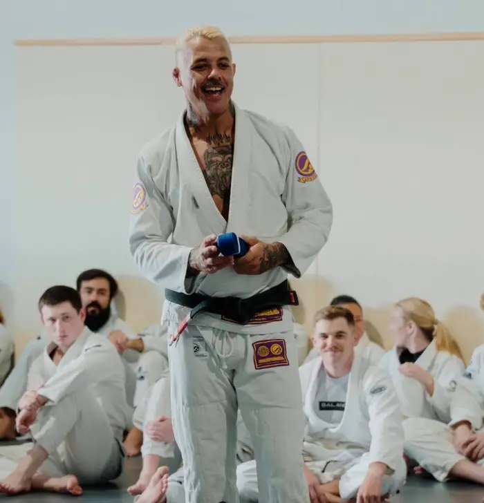 A black-belt coach addressing seated students in gis during a Balance BJJ session