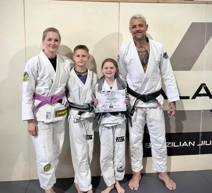 A young Balance BJJ student receiving a grading certificate with coaches and family