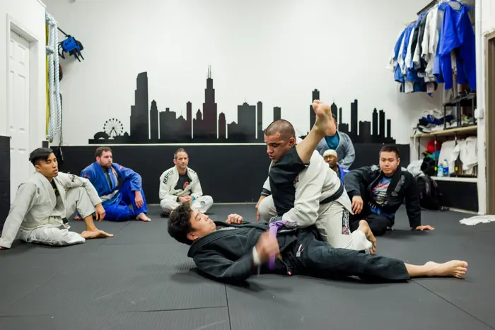Instructor demonstrating a Jiu-Jitsu position to seated students in front of the Chicago skyline mural