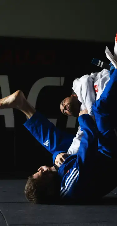 A gi Brazilian Jiu Jitsu sweep landing in front of the gym wall graphics