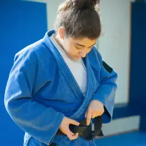 Young Close Quarters students grappling in front of the academy logo wall