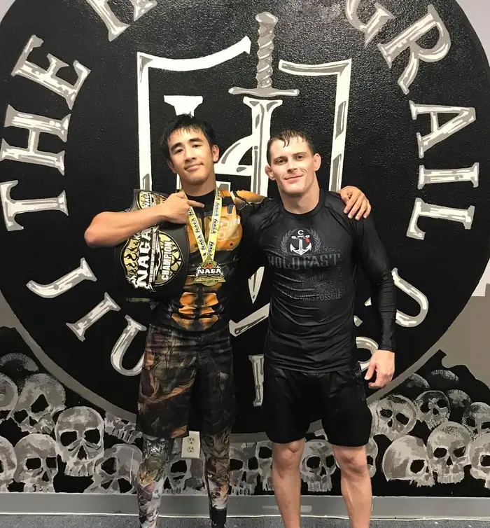 Holy Grail athlete pointing skyward in his Holy Grail rashguard after a win