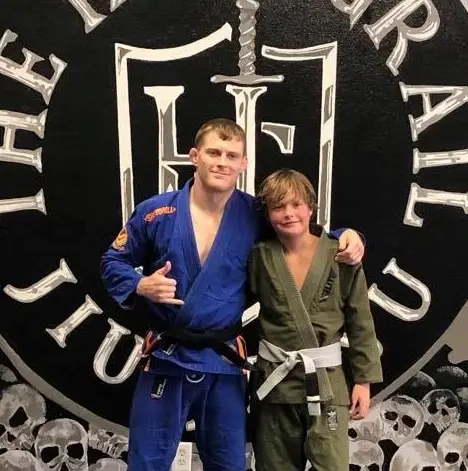 Coach Jordan Holy with a young belted student in front of the Holy Grail wall logo