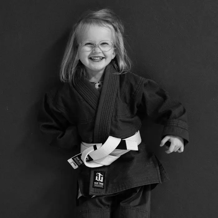 A young child smiling in a BJJ gi and white belt at VBC's kids program